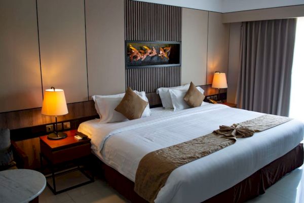 A cozy hotel bedroom with a large bed, two bedside tables with lamps, a decorative wall feature, and a window with curtains.