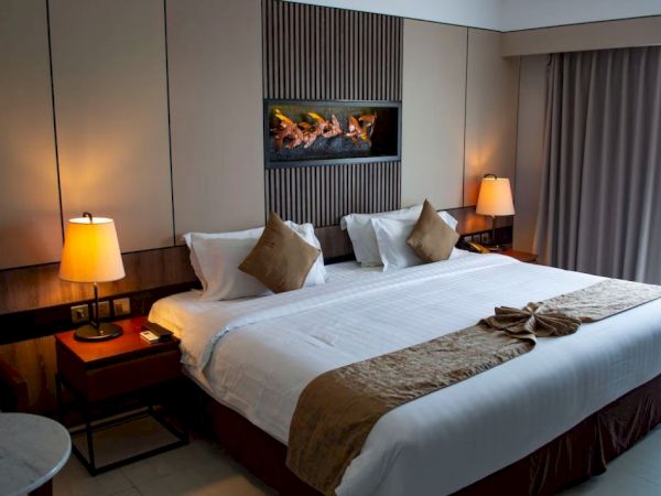 A cozy hotel bedroom with a large bed, two bedside tables with lamps, a decorative wall feature, and a window with curtains.