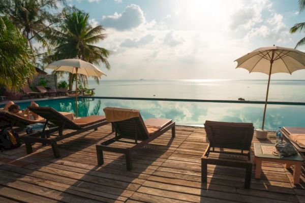 A serene poolside scene with lounge chairs, umbrellas, and a stunning view of the ocean under a bright sky with scattered clouds.