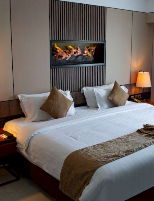 This image shows a modern hotel room with a large bed, bedside tables with lamps, a wall-mounted fireplace, and curtains covering a window.