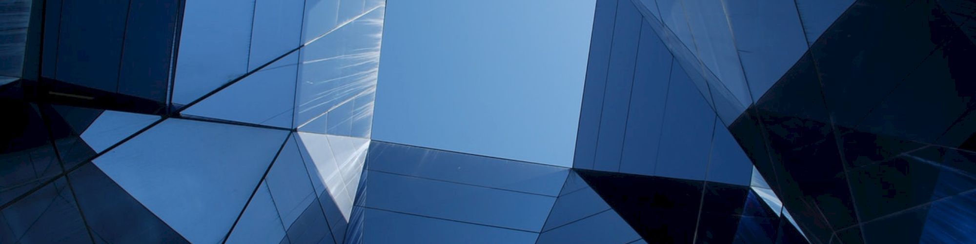 The image features a geometric arrangement of reflective glass panels forming an abstract, symmetrical pattern with a clear blue sky at the center.