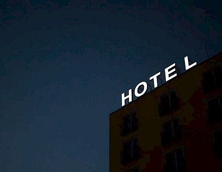The image shows the illuminated sign of a hotel at night, with some windows visible on the hotel's exterior wall.