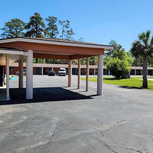 The image shows a motel with an outdoor parking area, several parked cars, and a palm tree. It is a sunny day with clear skies.