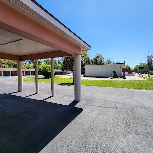 The image shows an outdoor parking area under a pink-roofed structure with posts, parked cars, and a view of a building and street beyond.