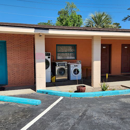 The image shows the outdoor area of a building with three doors and a washing machine and dryer setup. It appears to be a motel.