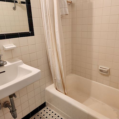 The image shows a bathroom with a white tiled bathtub, a sink with a faucet, a mirror above the sink, and a tiled floor.