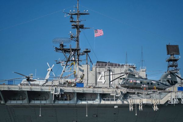 A military ship with two helicopters on deck, and an American flag flying on top.