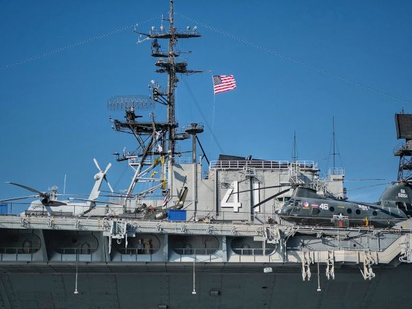 A military ship with two helicopters on deck, and an American flag flying on top.