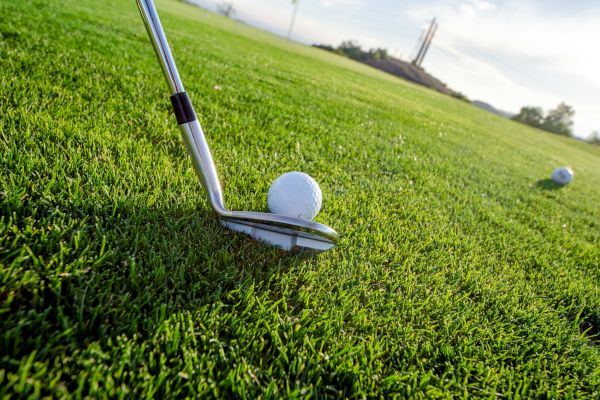 A close-up of a golf club next to a golf ball on a well-maintained green field, with another golf ball in the background.