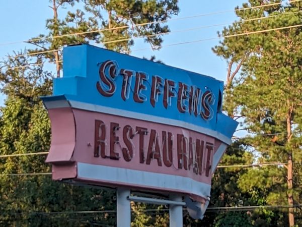 The image shows a vintage roadside sign with the text "STEFFENS RESTAURANT" in front of a backdrop of trees and overhead utility lines.