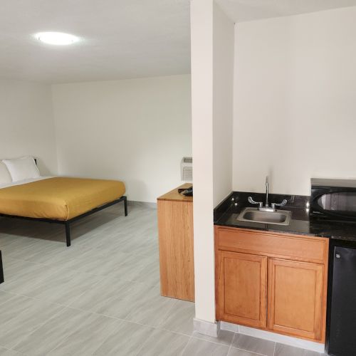 The image shows a motel room with two beds, a kitchenette with a sink, microwave, and mini-fridge, and basic furnishings.