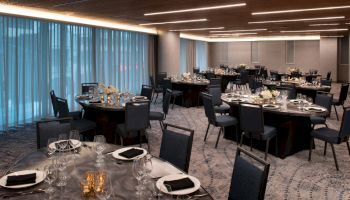 The image shows an elegant banquet hall with round tables set for an event, with black chairs and dim lighting.