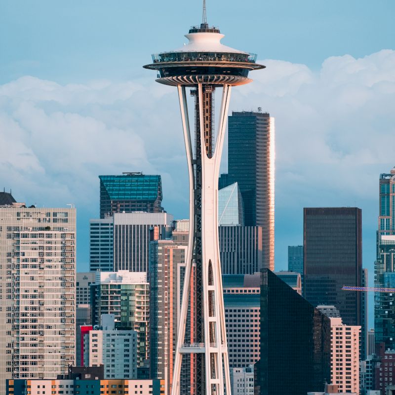 The image shows the Space Needle in Seattle, Washington, with various high-rise buildings in the background under a cloudy sky.