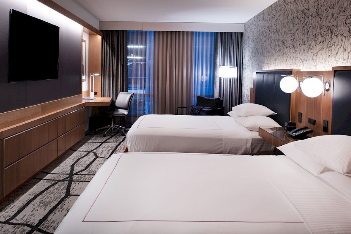 A modern hotel room with two beds, a flat-screen TV, a work desk, and contemporary decor.