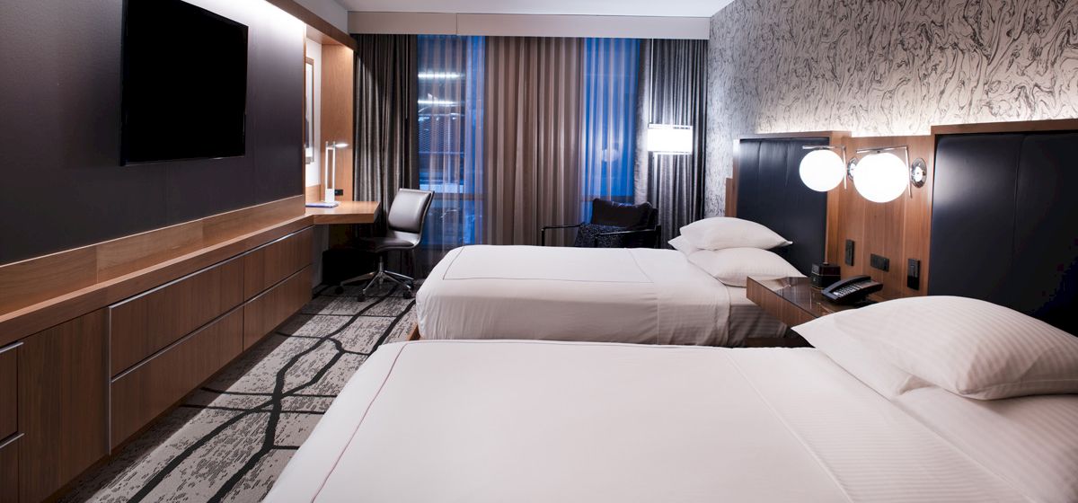 A modern hotel room with two beds, a flat-screen TV, a work desk, and contemporary decor.
