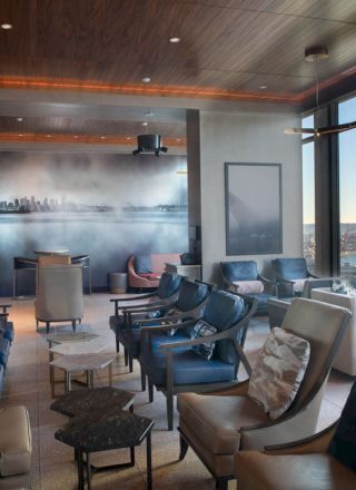 A modern lounge with comfortable seating, large windows offering an expansive water view, and a mural of a city skyline on the back wall.